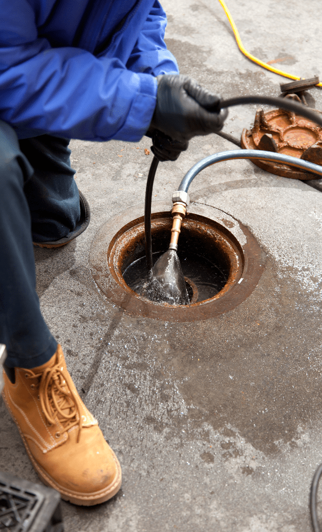 Worker in blue overalls feeding a hose into an open outdoor drain